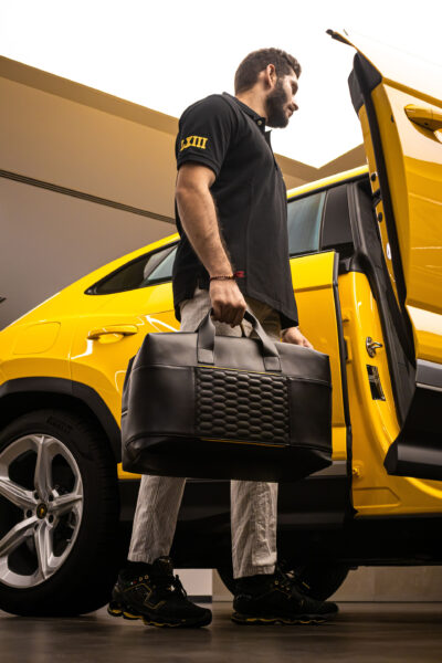 Man holding a travel bag getting into a Lamborghini Urus.