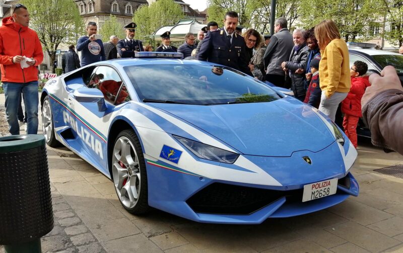 Sky blue Lamborghini Huracan parked at an event with people checking it out and police officers around it.