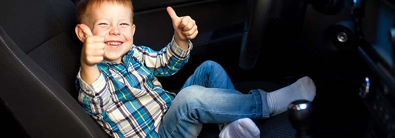 Kid in the drivers seat of a sports car with a black interior giving a thumbs up.