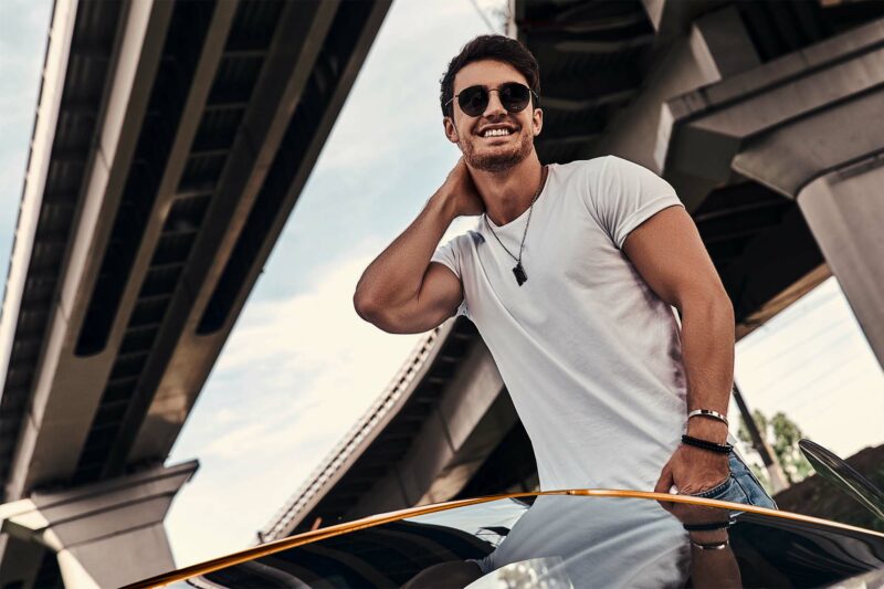 Young man standing over his yellow Lamborghini with sunglasses.