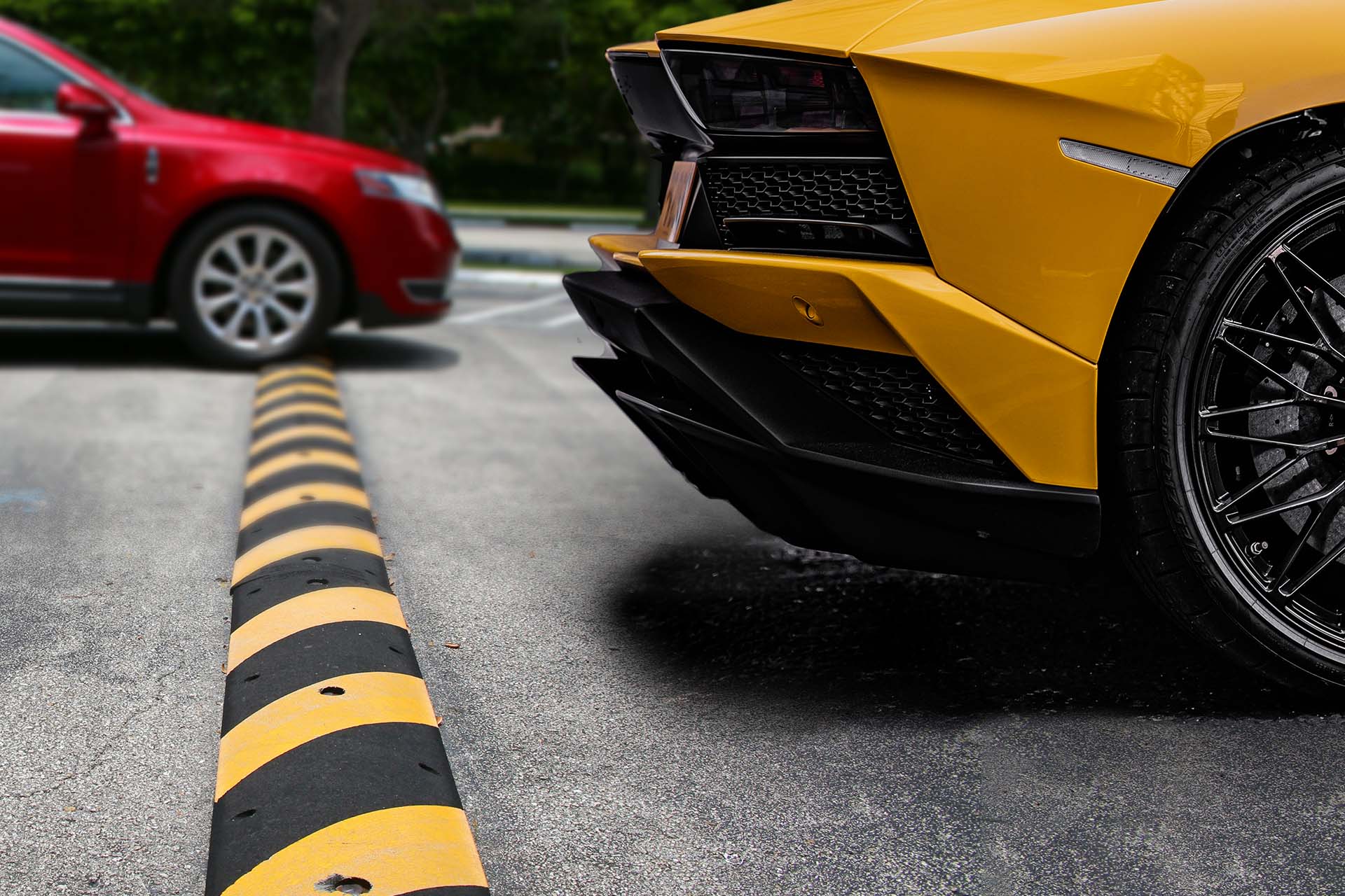 Yellow Lamborghini going over a speedbump with a red car behind it.