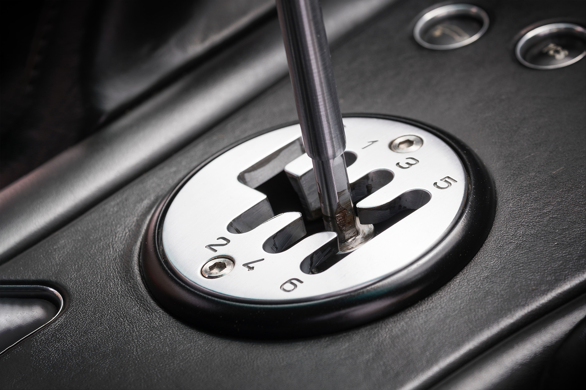 Silver gated manual transmission shifter in a supercar with a black leather interior.