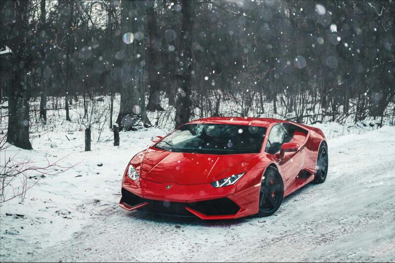 Red Lamborghini Huracan parked on a snowy road.