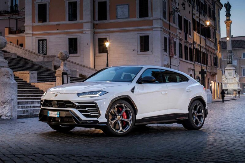 White Lamborghini Urus driving around a European city at dusk.