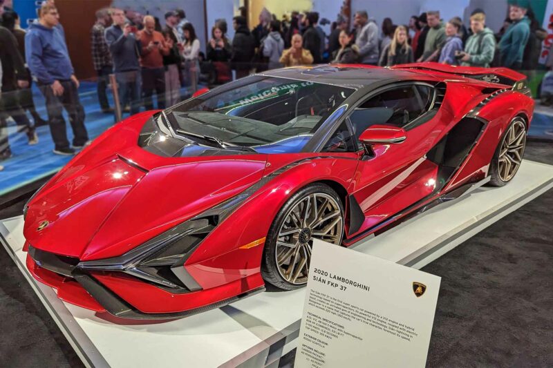 Red Lamborghini Sian three quarter view on a platform at an autoshow.