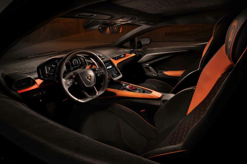 Lamborghini Revuelto interior from the driver side. Charcoal with orange accents. Racing steering wheel shape.