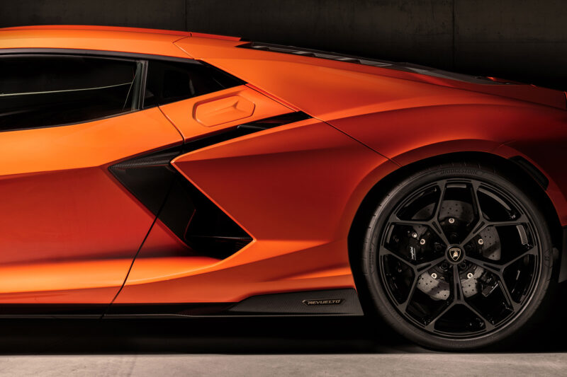 Photo of the side intake and gas filler cap and rear wheel of an orange Lamborghini Revuelto supercar.