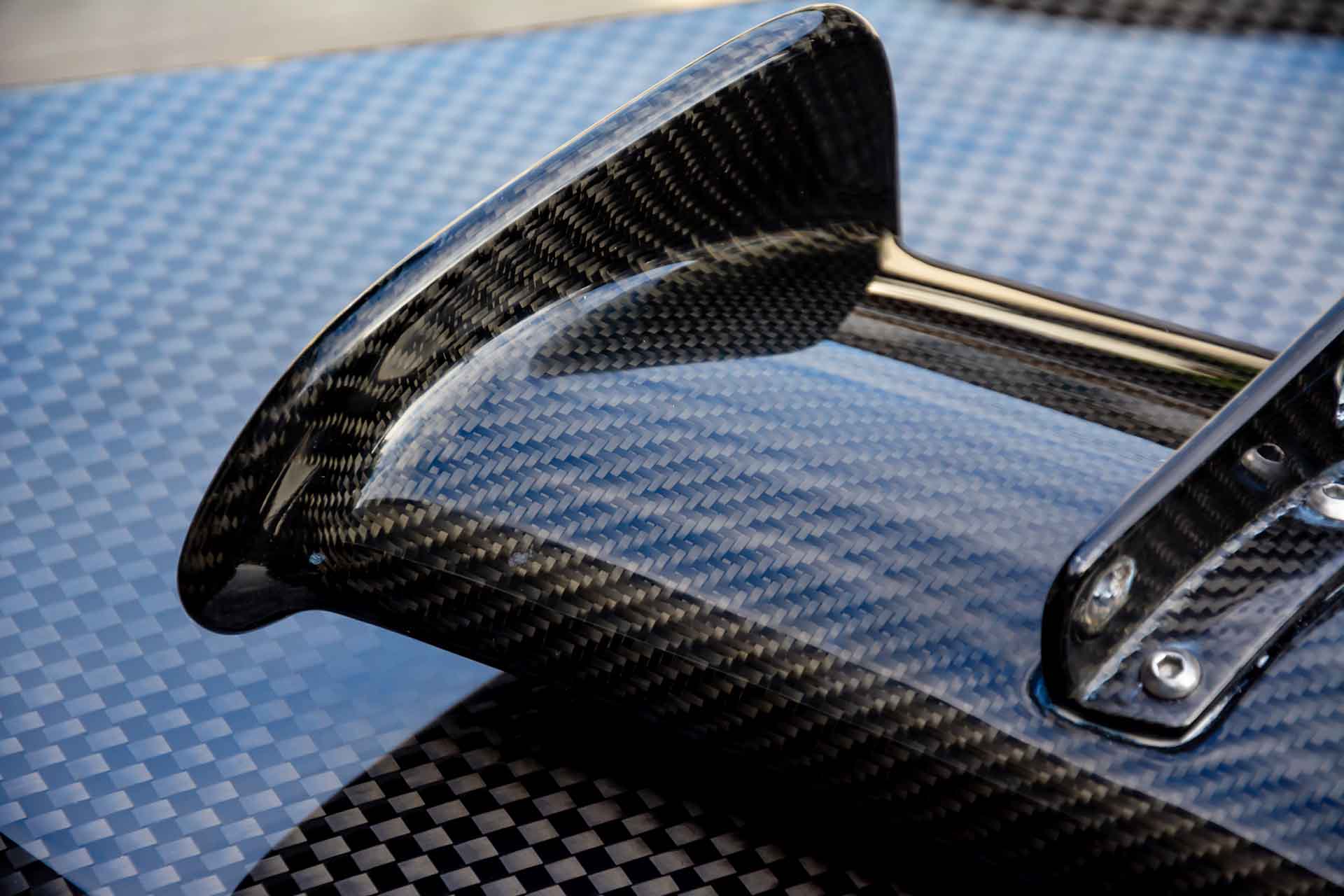 A carbon fiber wing from a supercar laying down upside down on a hood also made of carbon fiber.