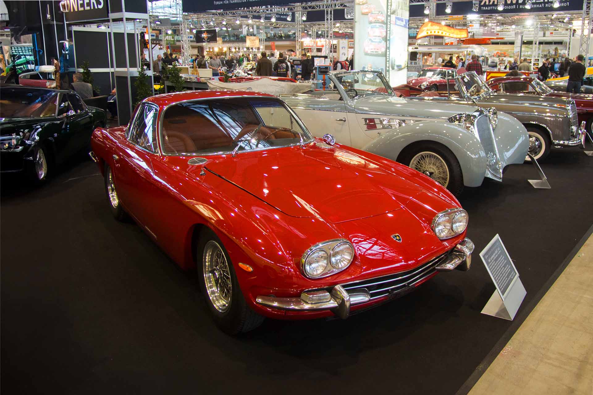 Red Lamborghini 400 GT displayed in an auto show with other classic cars.