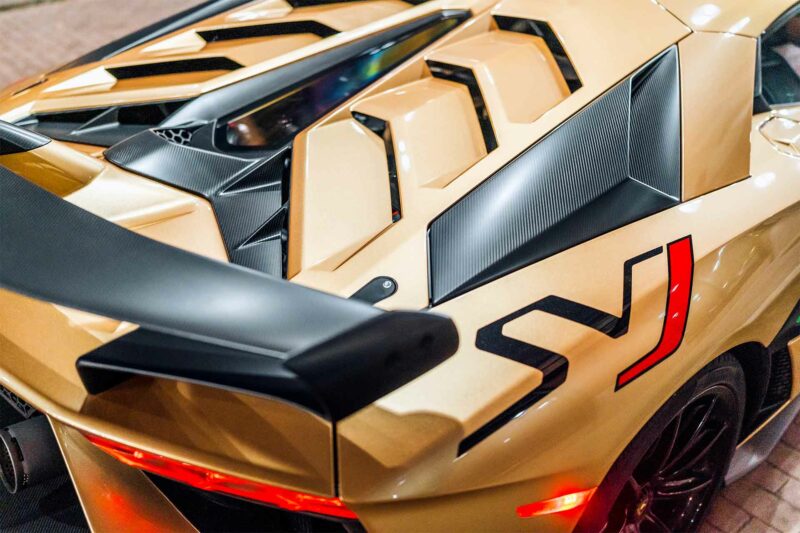 Quarter panel, hood, and rear wing of a gold Lamborghini Aventador SVJ.