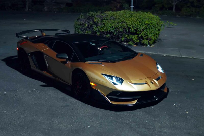 Gold Lamborghini Aventador at night packed in a parking log in a park.
