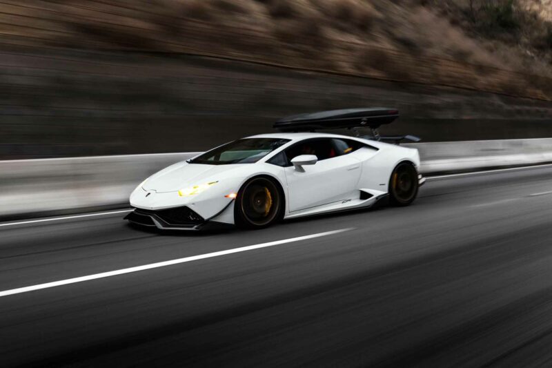 White Lamborghini Huracan with a storage attachment driving on the highway with a hill in the background.